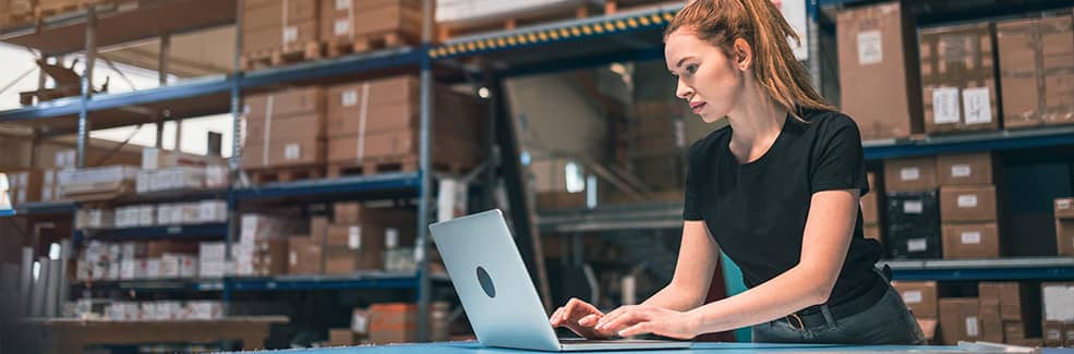 A woman using a laptop in a warehouse environment