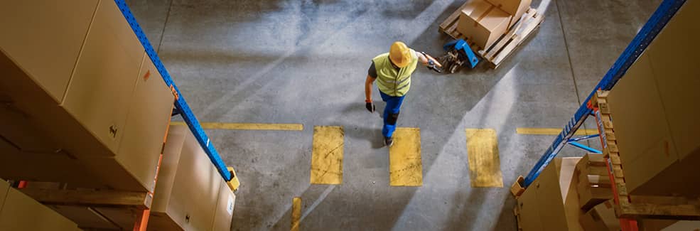 A worker viewed from top-down crossing a banded lane while pulling a manual lift